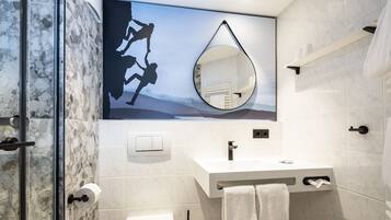 A modern bathroom with a glass shower enclosure, a white sink with a towel rack, and a large mirror.