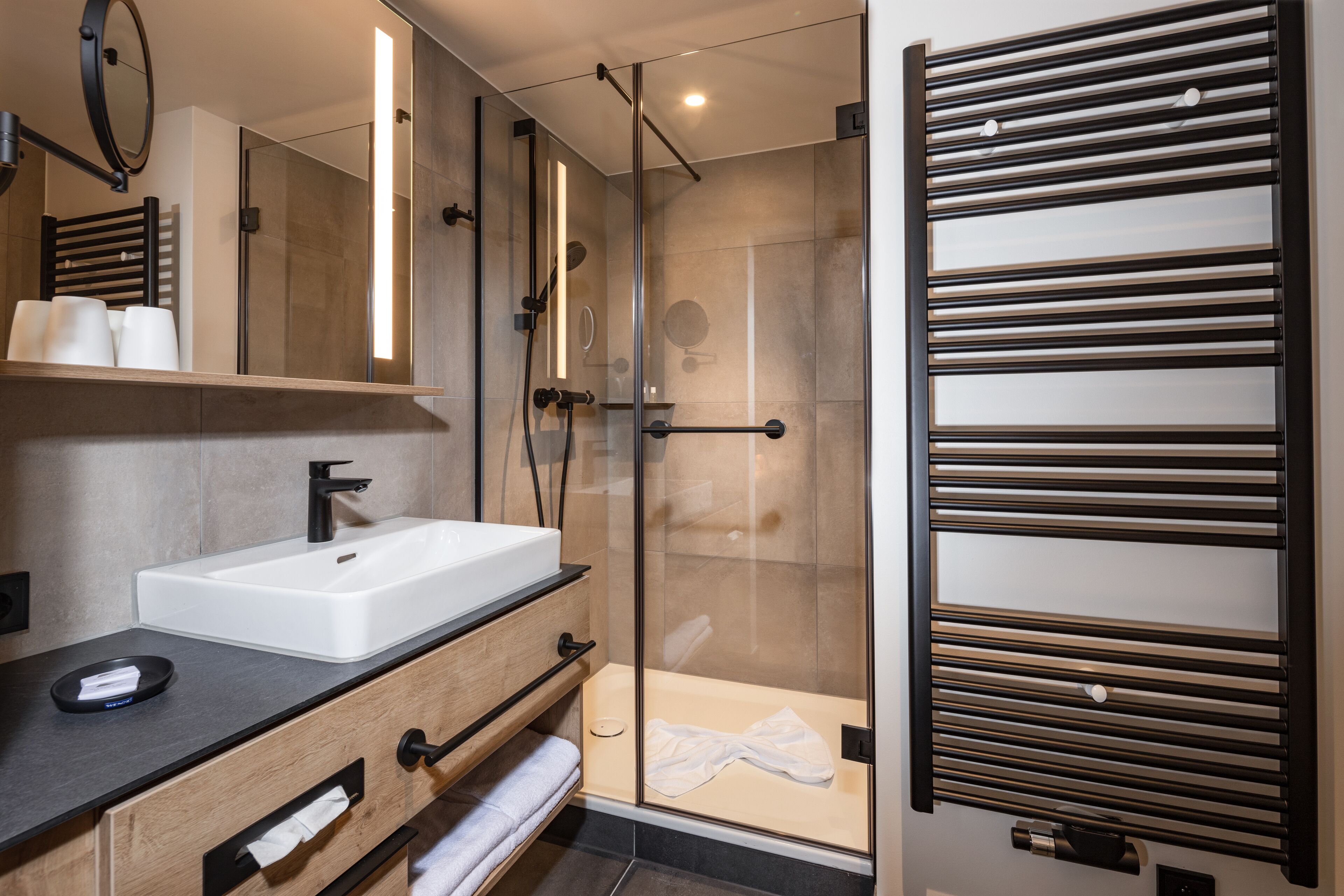 Un baño moderno con ducha de mampara de vidrio, un lavabo blanco y un perchero para toallas.