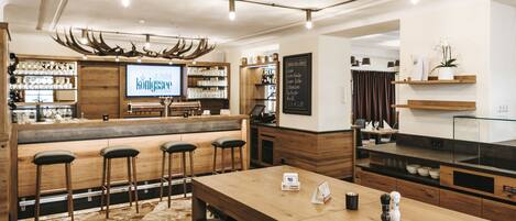 A bar area with wooden stools, a long table, and a television screen displaying a menu.
