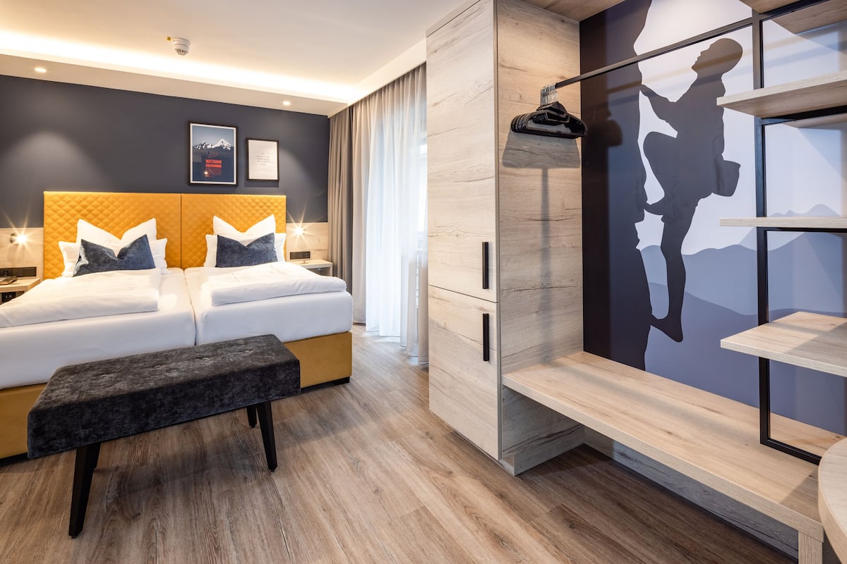 A modern hotel room with a large bed, a bench, a wardrobe, and a wall with a mountain silhouette.