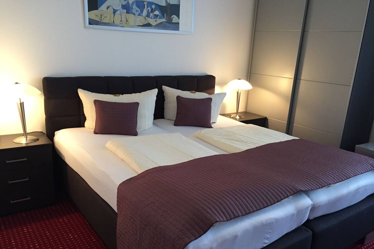 Un lit bien fait, avec une tête de lit sombre, du linge de lit blanc et deux lampes de chevet.