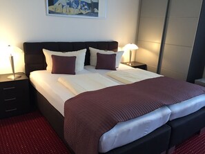 Un lit bien fait, avec une tête de lit sombre, du linge de lit blanc et deux lampes de chevet.