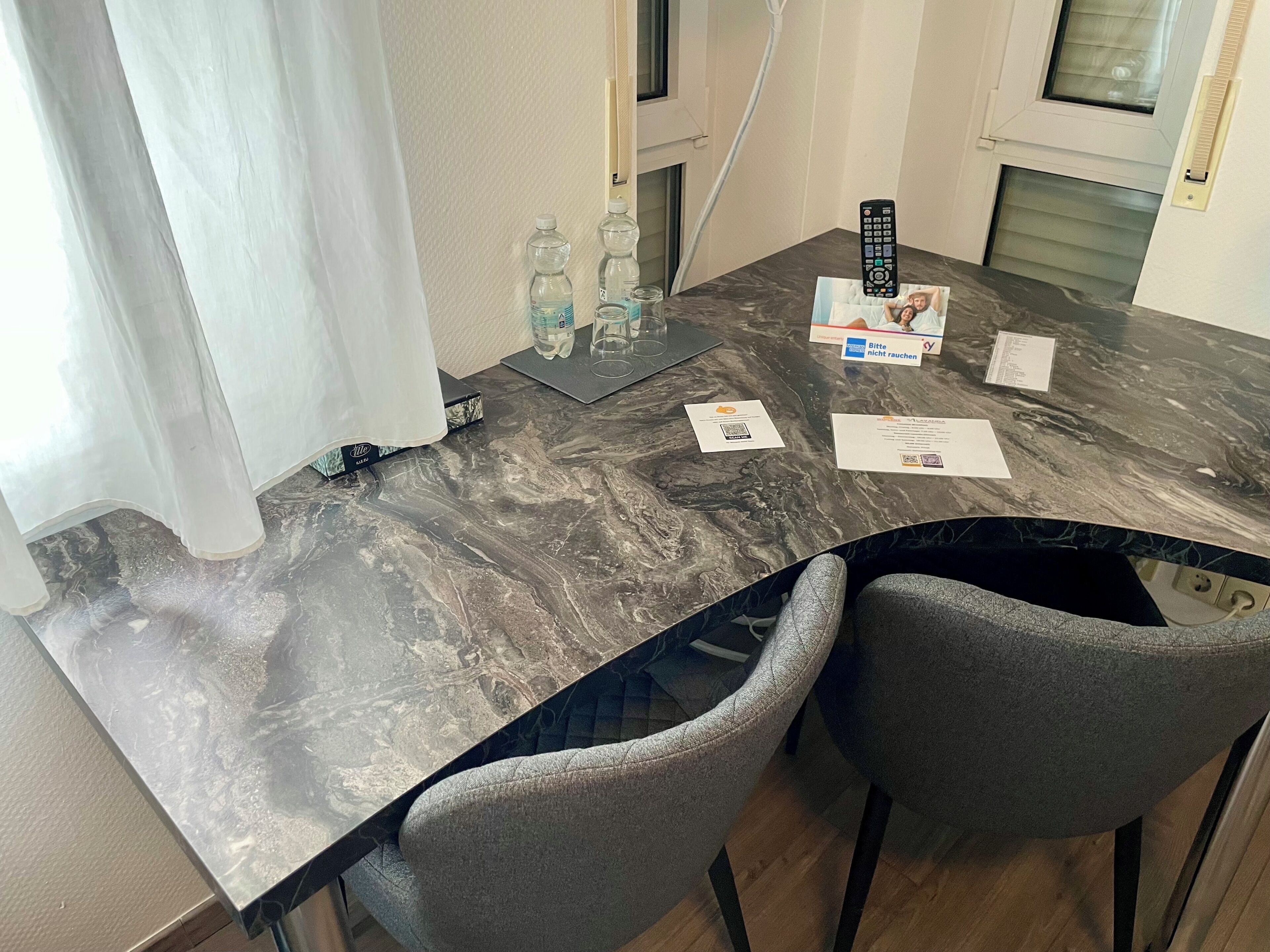 A dining table with a marble top, two grey upholstered chairs, a remote control, and some papers on the table.