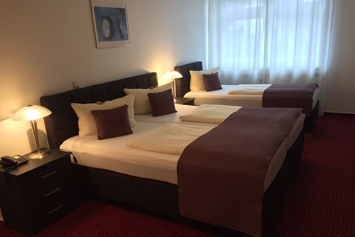 Une chambre d’hôtel avec deux lits, un bureau avec une lampe, un téléphone et une fenêtre avec des rideaux.
