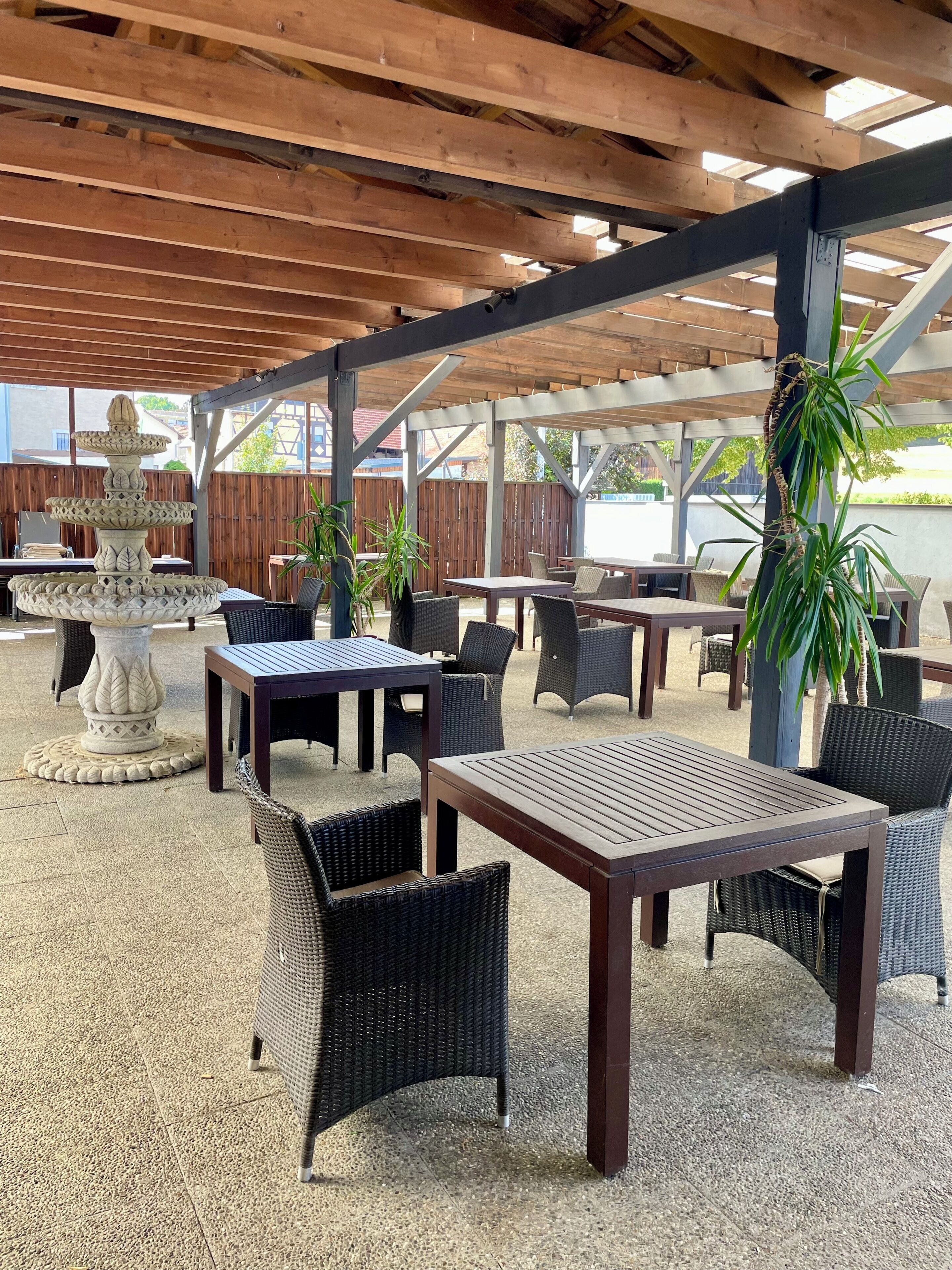 Ein möblierter Patio mit Tischen, Stühlen, einer Zierfigur-Fontäne und Pflanzkübeln.