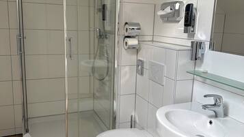 Ein modernes Badezimmer mit einer gläsernen Duschkabine, einer weißen Toilette und einem Waschbecken mit Spiegel darüber.