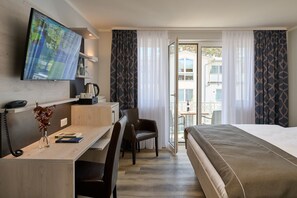 A hotel room with a bed, desk, chair, TV, and a view of the outside balcony. - R&R Strandhotel Baabe (Ostseebad Baabe)