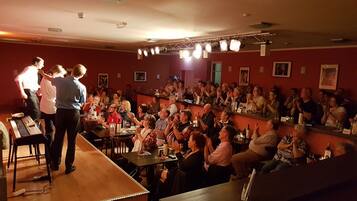 Eine Bar mit einer Bühne für Auftritte, Tischen mit Getränken und sitzenden Gästen.