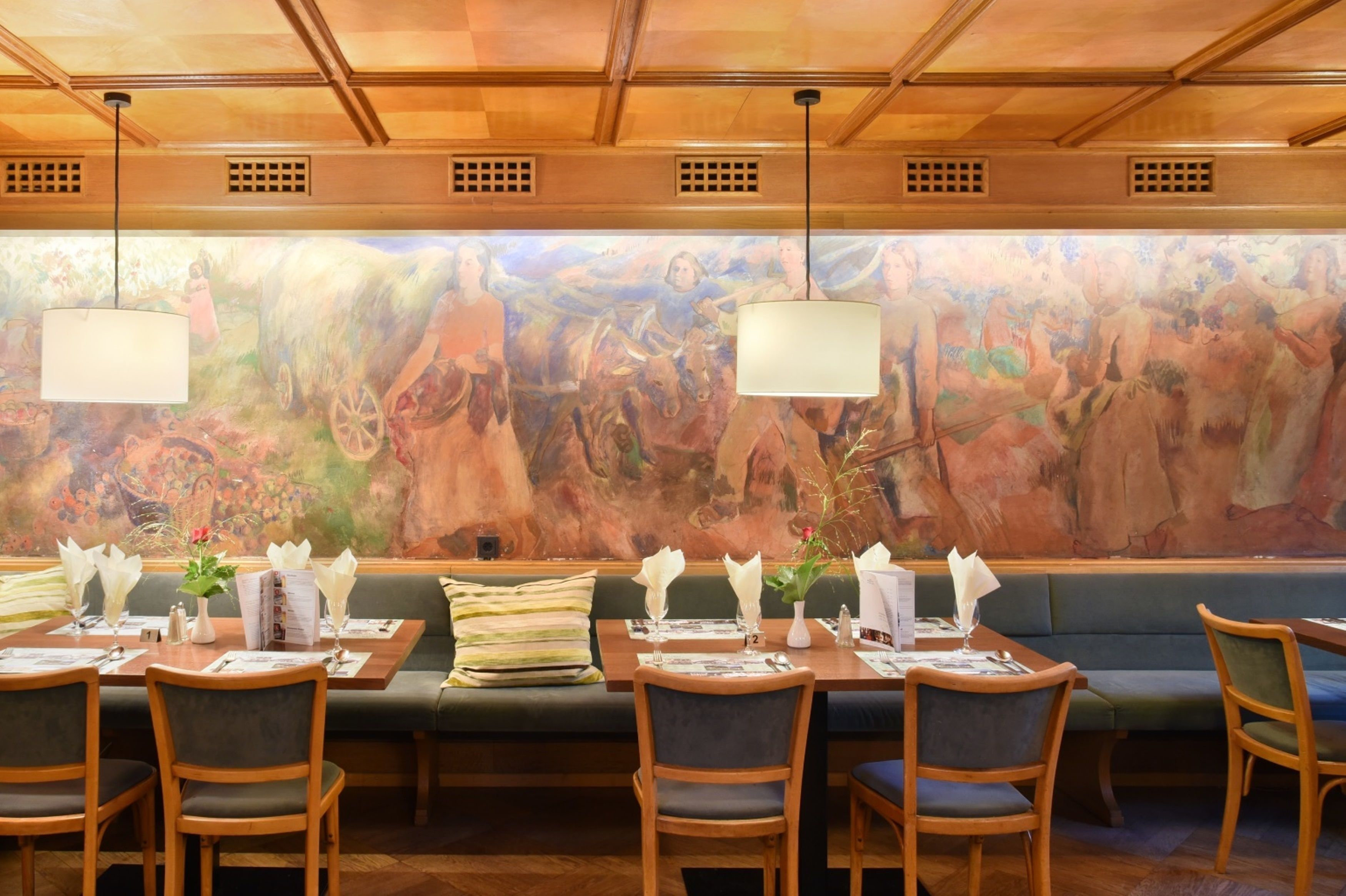 A restaurant with a mural on the wall, wooden tables and chairs, and hanging pendant lights.