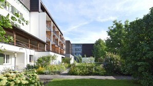 A modern building with multiple balconies, a garden area with various plants, and a clear sky.