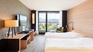 A hotel room with a bed, a desk, a TV, a balcony with a view, and a chair.