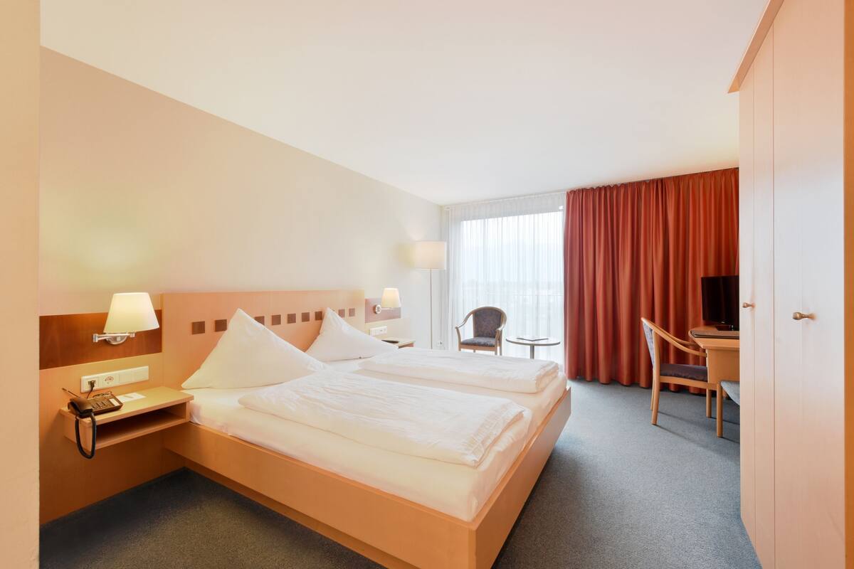 A hotel room with two beds, a desk, a chair, a TV, and a window with curtains.
