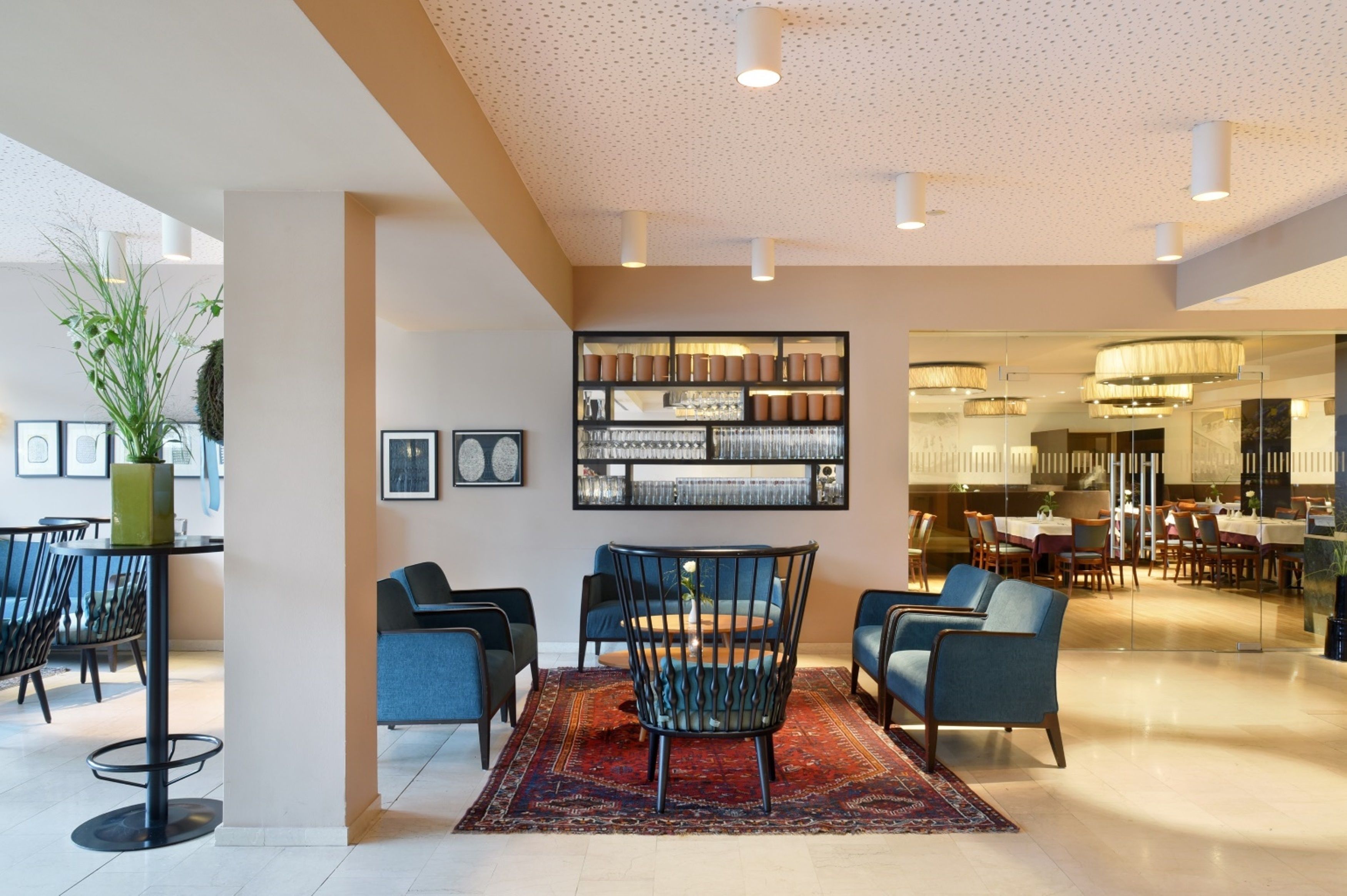 Un hall d’hôtel moderne comprenant un espace repas, une bibliothèque et un grand miroir qui reflète l’espace repas.