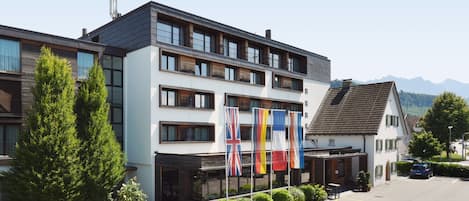 A modern hotel with multiple floors, flags, and a parking area.