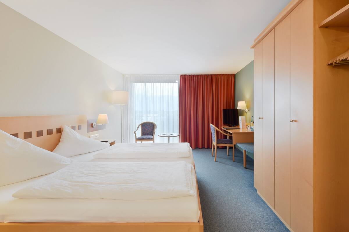 A hotel room with two beds, a desk, a chair, a television, and a wardrobe.