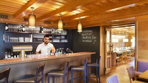 A bar area with a bartender, shelves with bottles and glasses, and a chalkboard menu.