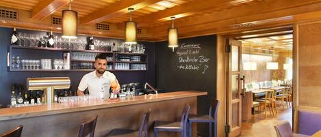 A bar area with a bartender, shelves with bottles and glasses, and a chalkboard menu.