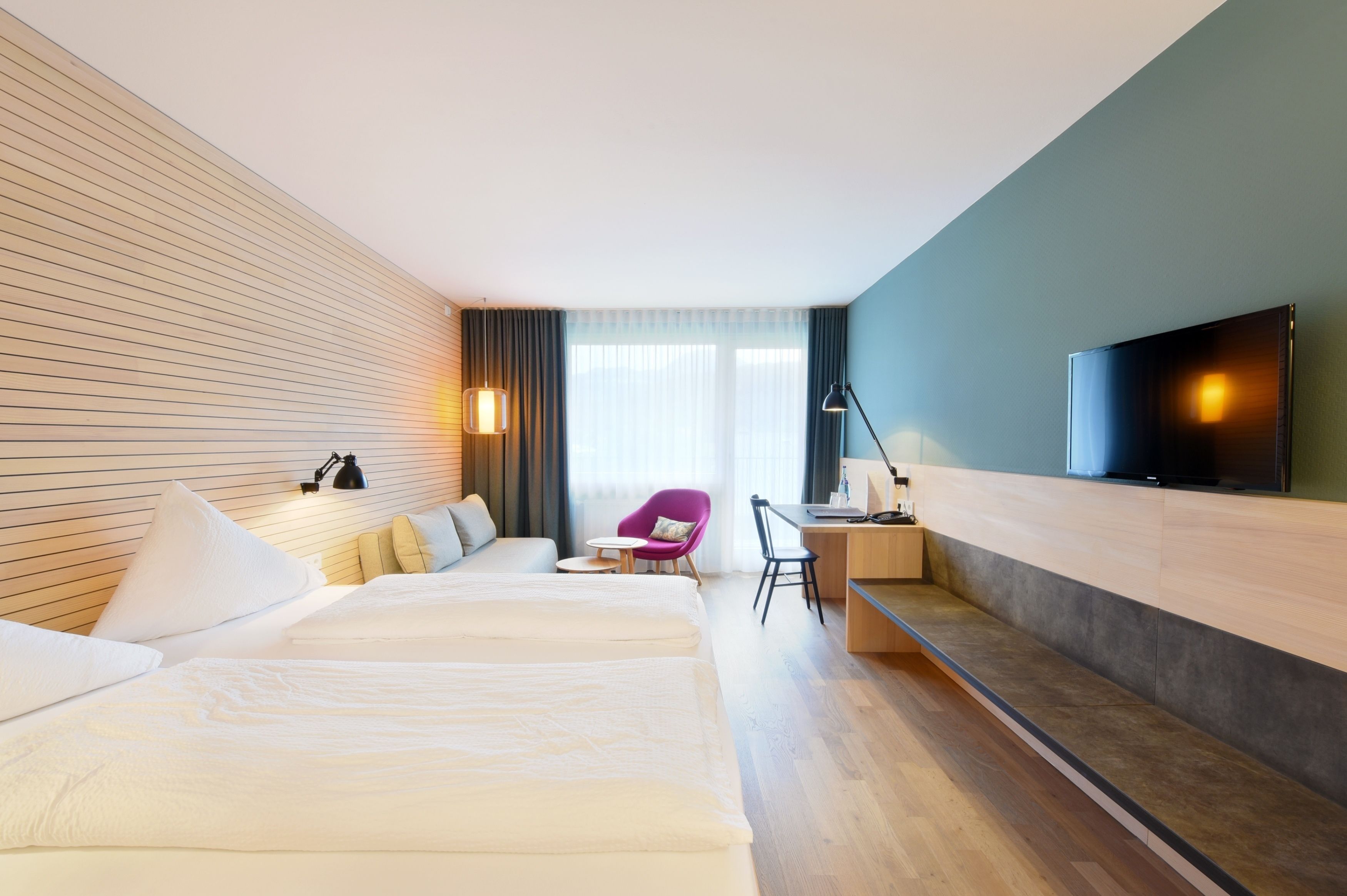 Habitación de hotel con dos camas, un escritorio, una silla, un televisor y una ventana con cortinas.