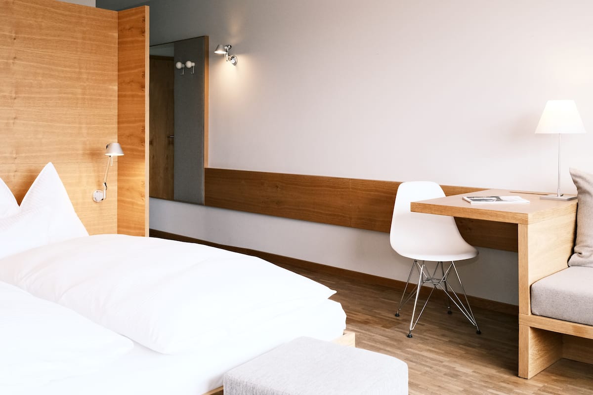 A hotel room with a bed, a desk, a chair, and a lamp.