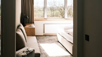 A hotel room with a bed, a sofa, a window with curtains, a lamp, and a suitcase.