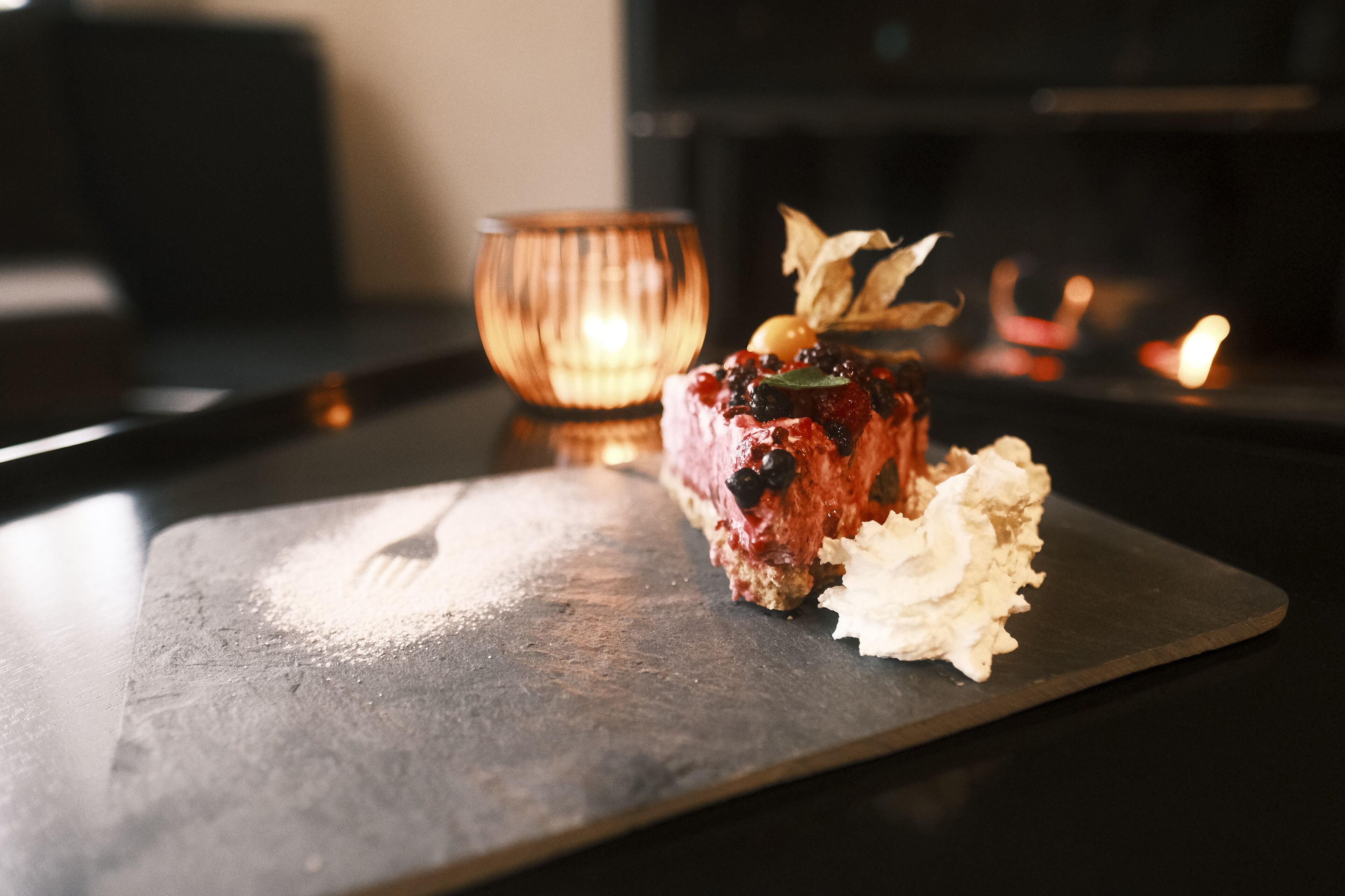 Un postre sobre un plato de pizarra con una vela al fondo.