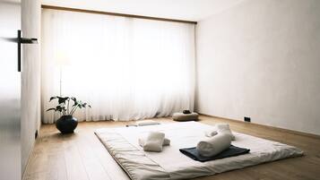 Habitación minimalista con esterilla de tatami, almohadas, una planta y una lámpara.