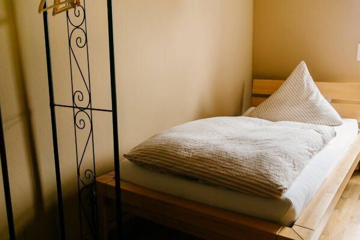 Una cama individual con estructura de madera y colchón blanco, con dos almohadas.