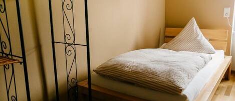 Una cama individual con estructura de madera y colchón blanco, con dos almohadas.
