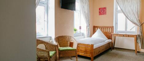 A bedroom with a wooden bed, a wicker chair, a desk, and a TV mounted on the wall.