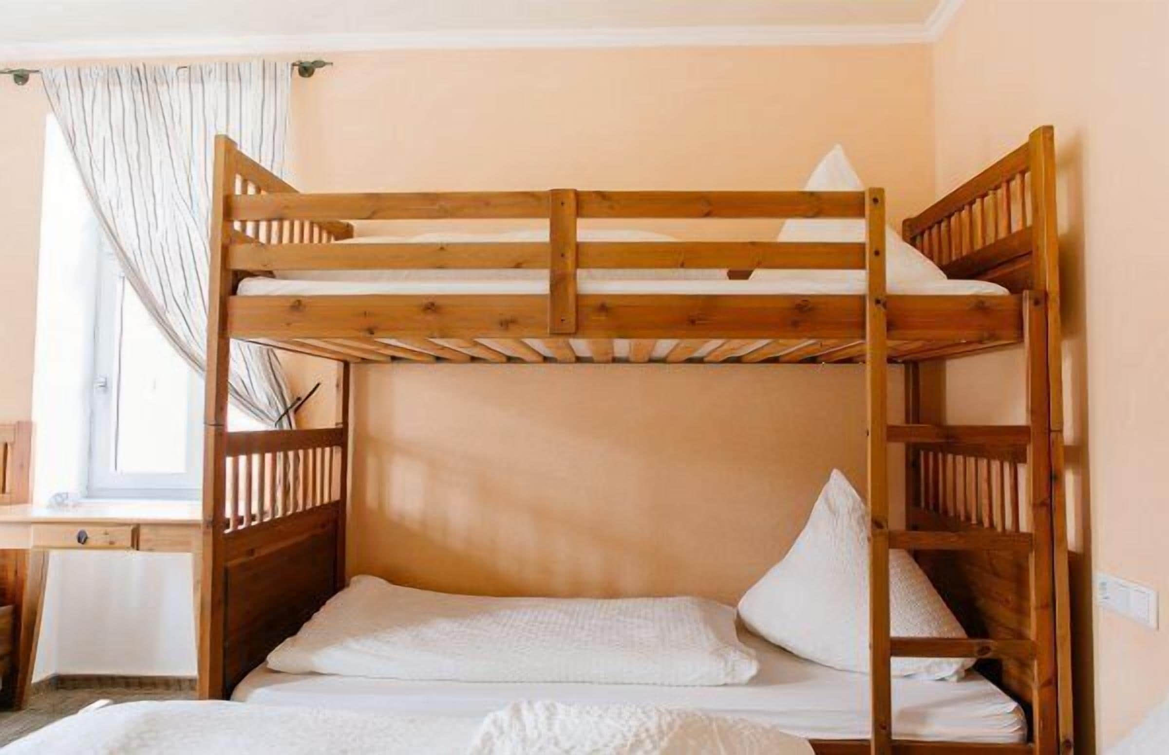 A bunk bed with a wooden frame and white bedding in a room with peach walls and a window with curtains.