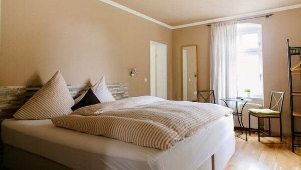 Un dormitorio con cama, una silla, una mesita y una ventana con cortinas.