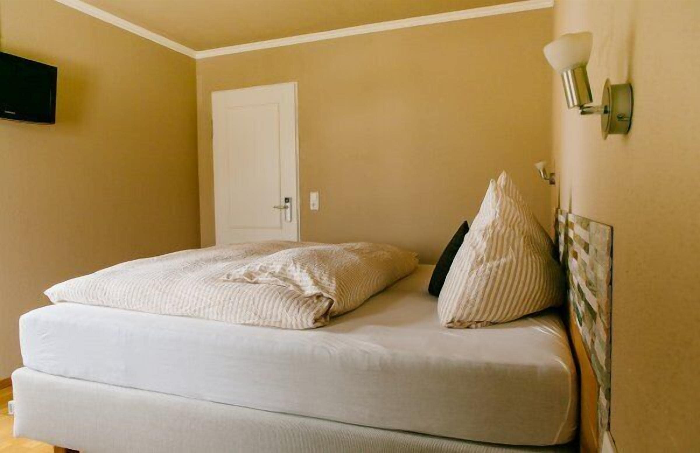 Un dormitorio con cama, una puerta y una lámpara fijada a la pared.