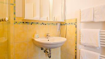 Un baño con un lavamanos blanco, un espejo y un perchero con toallas.