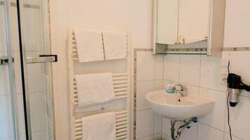 Un baño con cabina de ducha de vidrio, un lavabo blanco con espejo y un perchero con tres toallas.