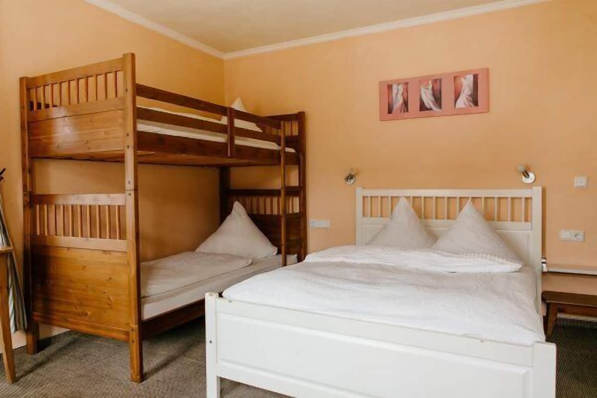Una habitación con literas y una cama individual, una pequeña mesa y un cuadro colgado en la pared.