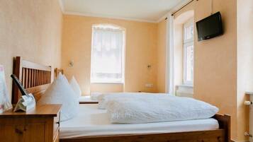 Cozy bedroom with a comfortable bed, television, and a nightstand with a lamp and reading material.