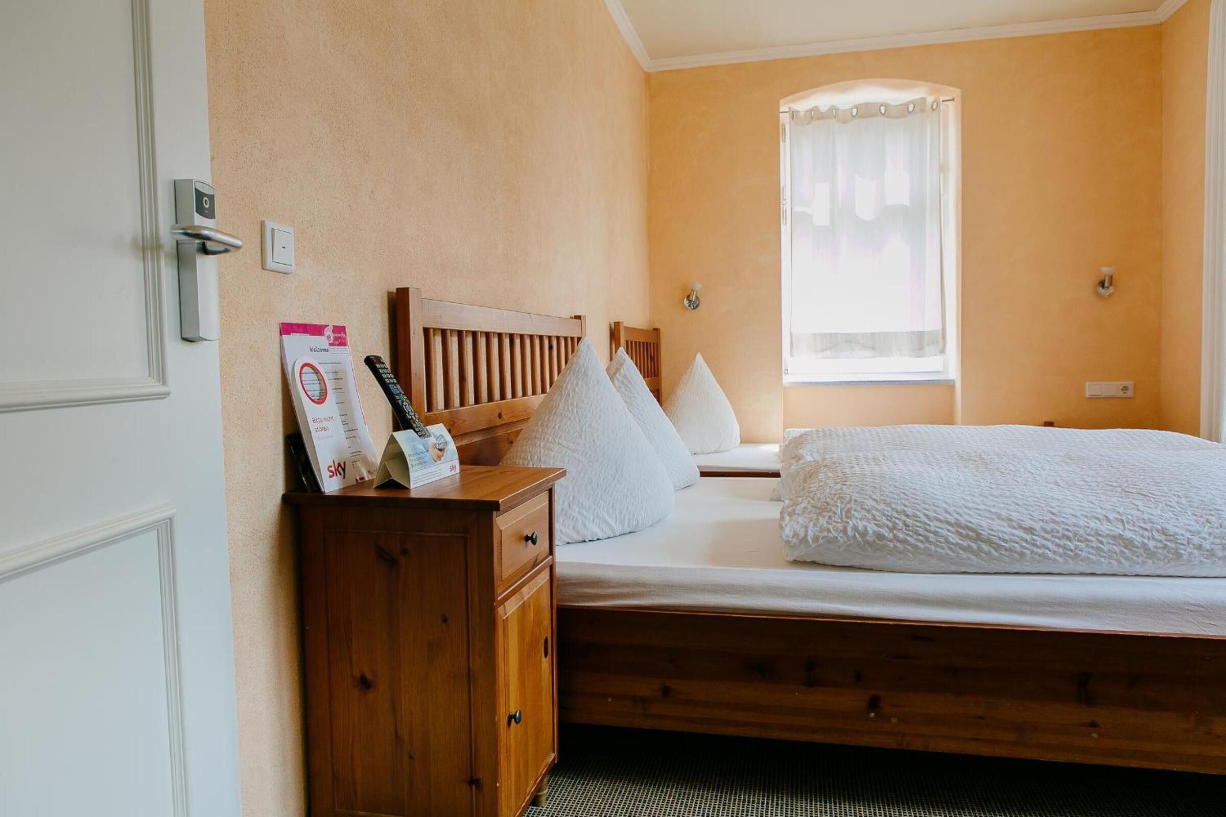 A bedroom with a wooden bed, a nightstand, a wardrobe, and a window with a sheer curtain.