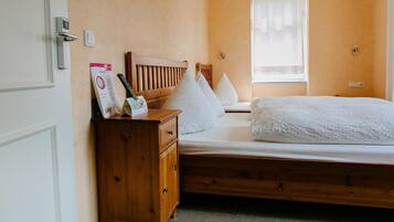 A bedroom with a wooden bed, a nightstand, a wardrobe, and a window with a sheer curtain.