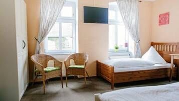 Een slaapkamer met een houten bed, twee rotan stoelen, een televisie en een raam met gordijnen.