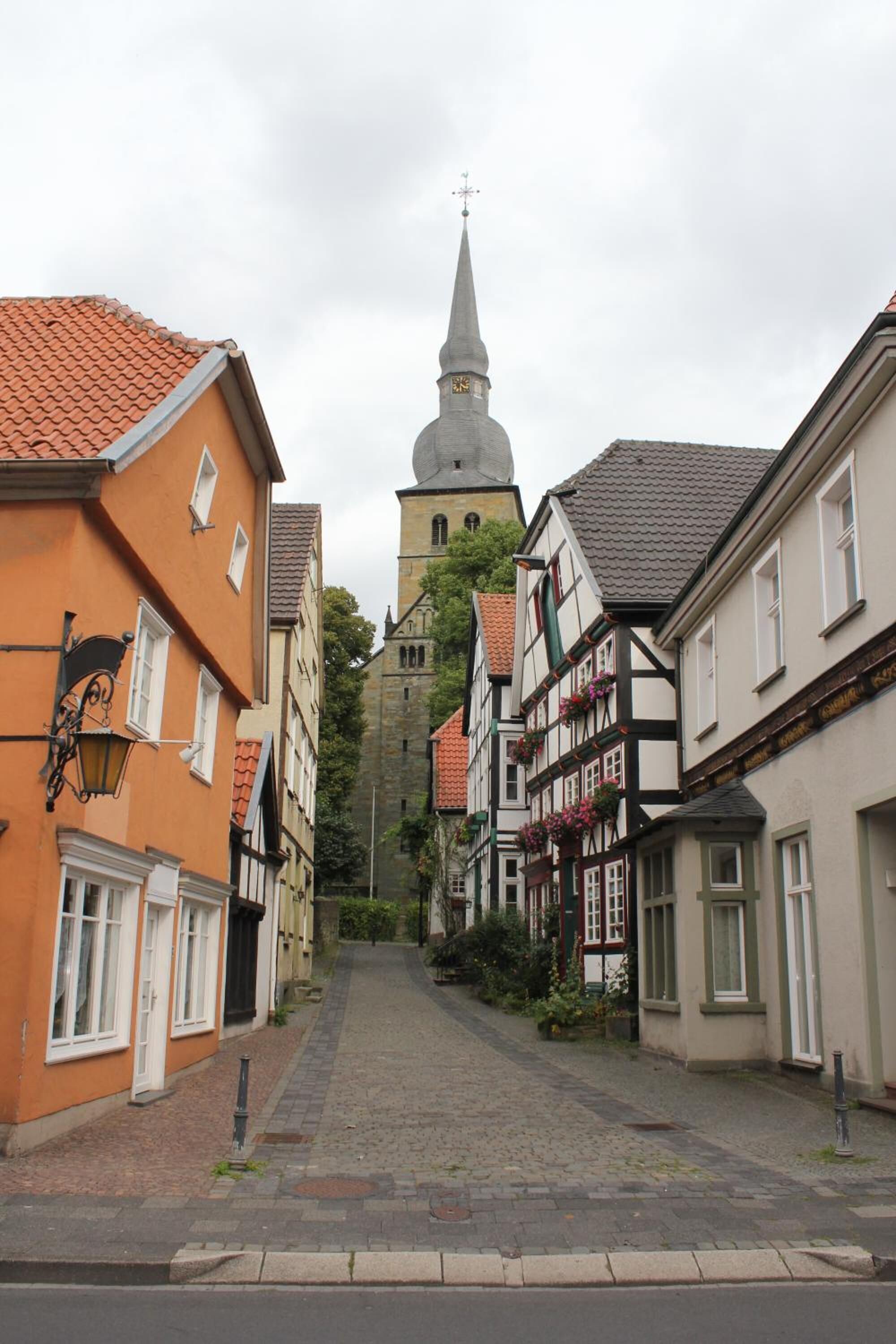 Eine enge Kopfsteinpflasterstraße, gesäumt von traditionellen Fachwerkhäusern, die zu einer Kirche mit einem hohen Kirchturm führt.