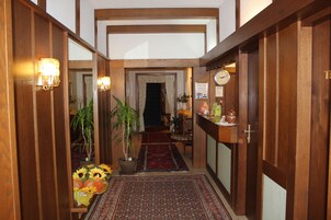 A wooden hallway with a red patterned rug, potted plants, and a clock on the wall.