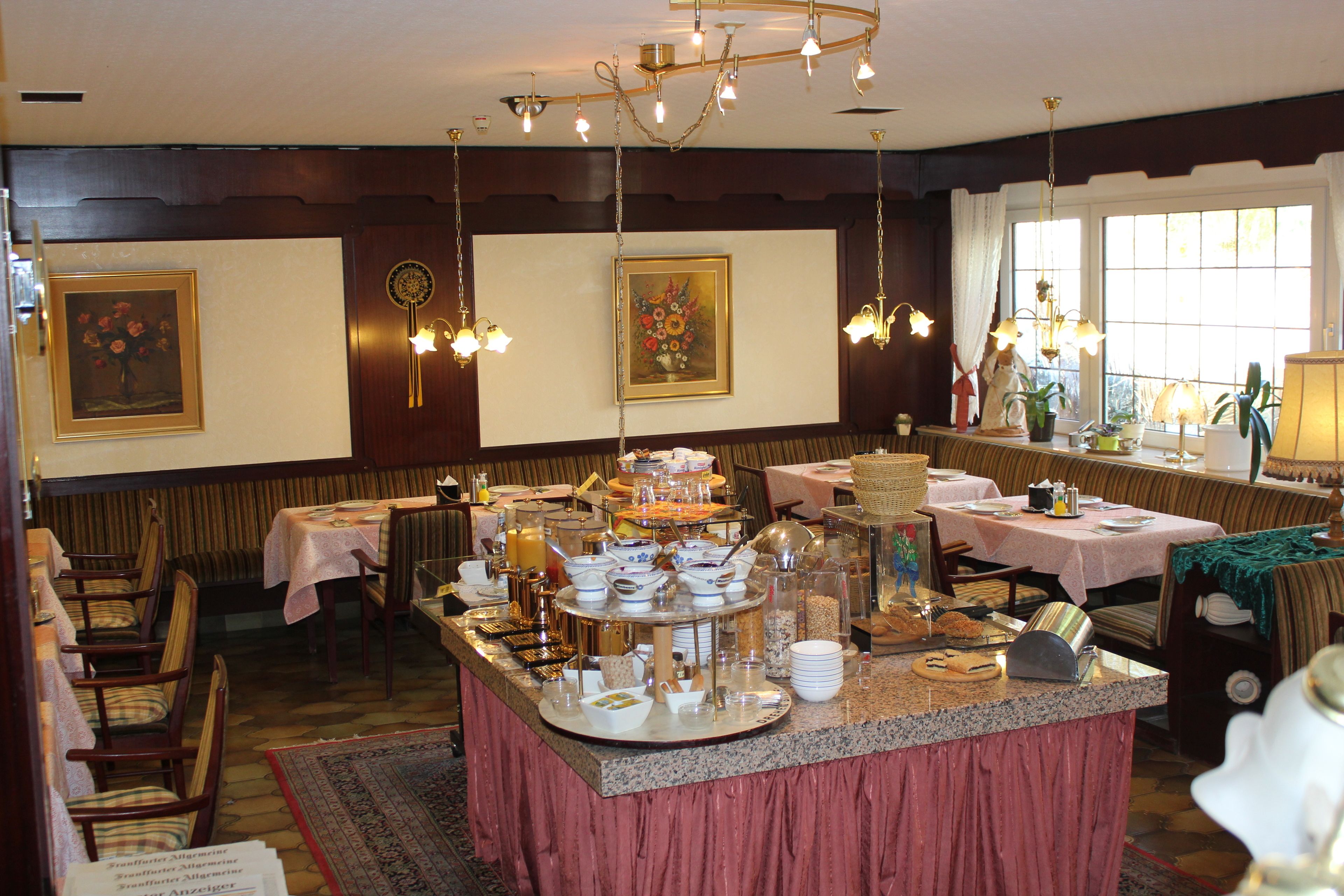 Ein Restaurant mit einer zentralen Buffet-Theke, mehreren Esstischen und einer Kristallleuchter.