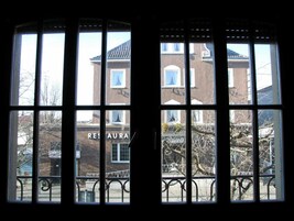 A view through a window with a metal railing, a building with a sign reading "RESTAURANT" in the background.