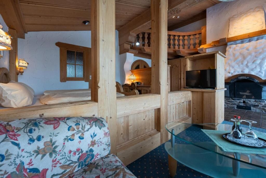 A cozy room with wooden walls, a bed, a sofa, a glass table, and a fireplace.