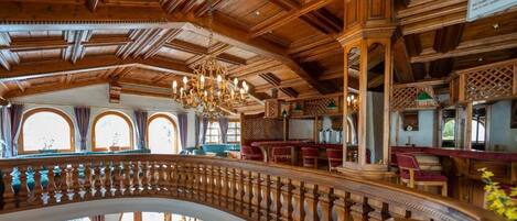 A grand interior with a high ceiling, ornate wooden beams, and a central staircase.