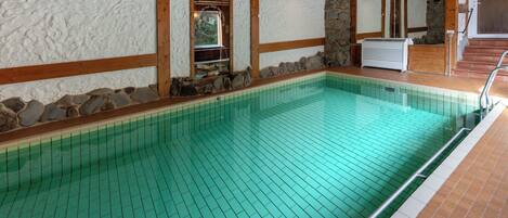 Une piscine intérieure avec des murs en pierre, des poutres en bois et un sol carrelé.