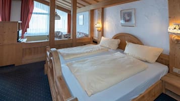 Cama doble con cabecera de madera, mesita de noche con lámpara y ventana con cortinas.