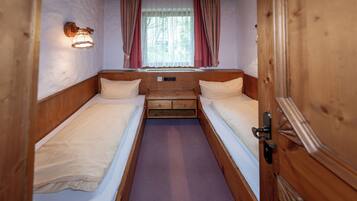 Quarto pequeno com duas camas individuais, janela com cortinas e luminária na parede.