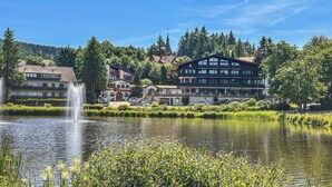 A lakeside hotel with a fountain, a church, and a mountain backdrop.