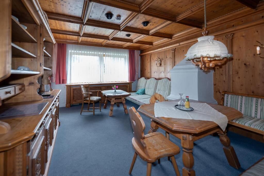 A wooden cabin interior with a dining table, chairs, a sofa, and a window with curtains.